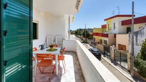 Ein Balkon mit Tisch und Stühlen, eine grüne Tür und Blick auf eine Straße mit Häusern.