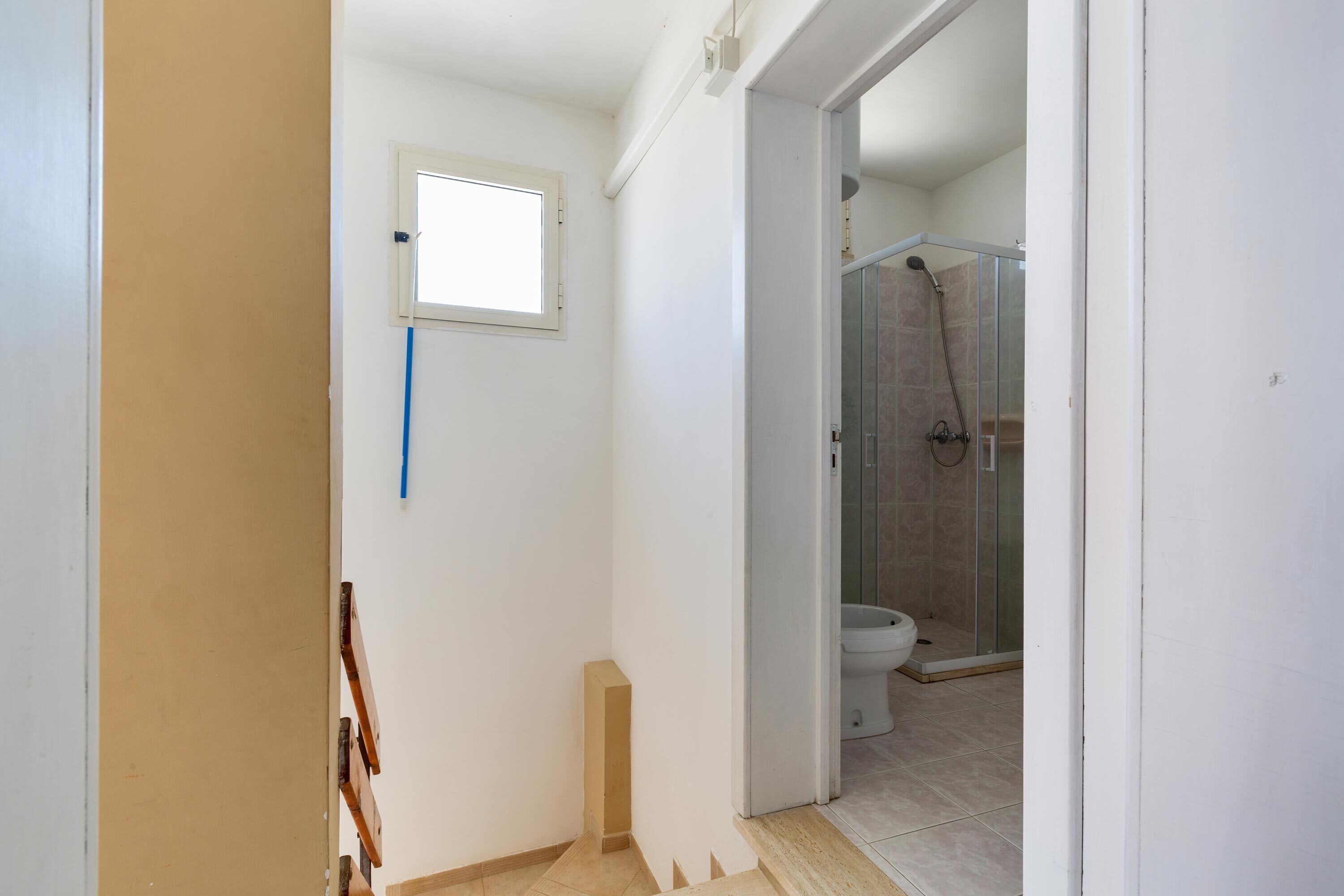 A bathroom with a shower, toilet, and a small window.