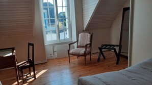 Een kamer met een schuine kap, een groot raam, een houten vloer, een bed, een stoel en een spiegel.