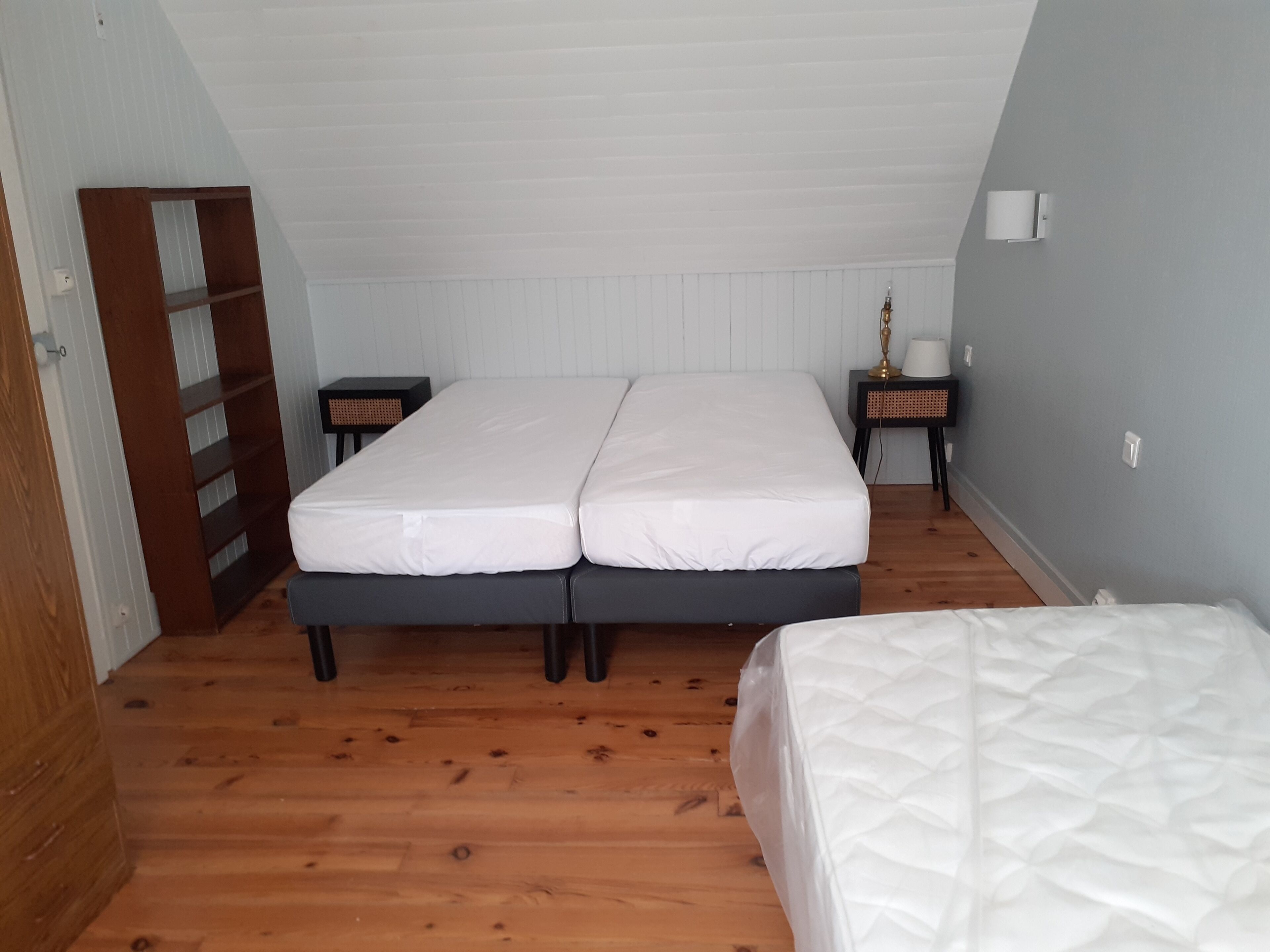 Een slaapkamer met twee bedden, houten vloeren, een klein nachtkastje met lamp en een kledingkast.