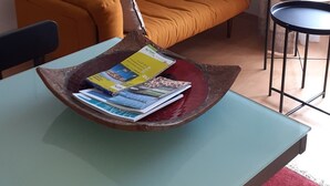 Een woonkamer met een bank, een salontafel met tijdschriften, een schilderij aan de muur, en een bijzettafeltje met een stoel.
