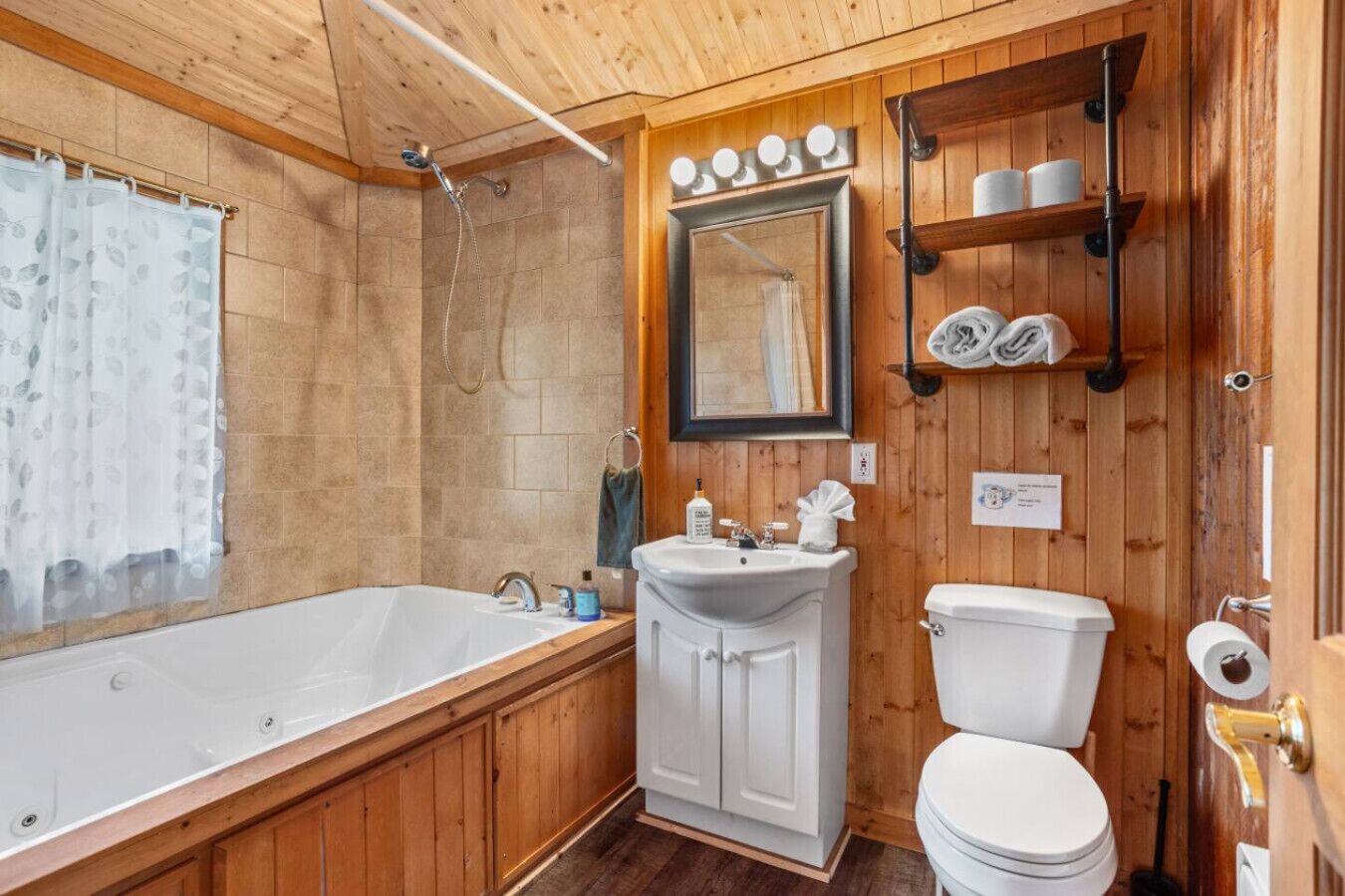 A wooden-paneled bathroom with a bathtub, sink, toilet, and a mirror.