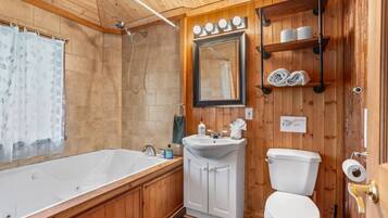 A wooden-paneled bathroom with a bathtub, sink, toilet, and a mirror.