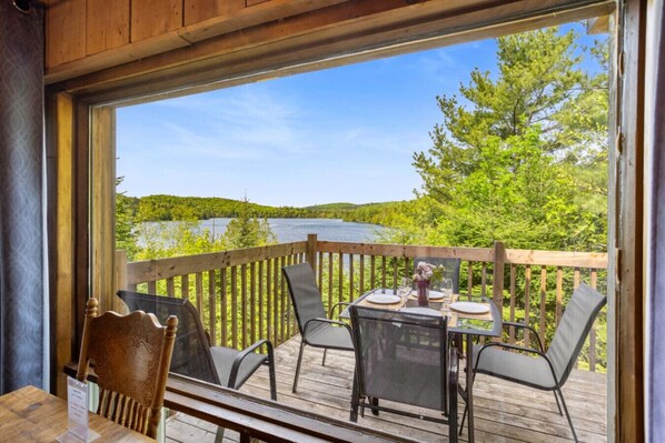 A deck with a table set for two, overlooking a lake and forest.
