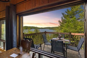 A wooden deck with a table and chairs, overlooking a lake and forested area.