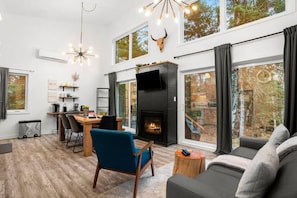 A modern living room with a fireplace, large windows, and a dining area. - Chalet avec spa privé à louer dans les Laurentides — Lac Sarrazin, Sainte-Lucie-des-Laurentides (Sainte-Lucie-des-Laurentides)