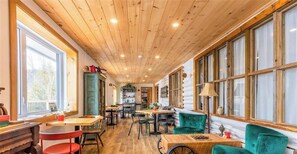 A cozy interior with wooden ceilings, large windows, and green upholstered chairs.