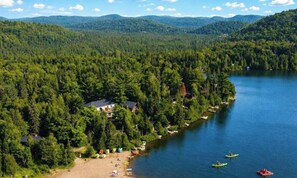 A lakeside property with a beach, kayaks, and a house surrounded by dense forest.