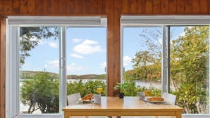 Een kamer met houten lambrisering, een ontbijttafel en uitzicht op een meer en bomen.