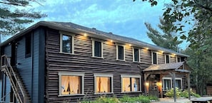 A log cabin with a covered porch, large windows, and a staircase leading to the entrance. - Mini chalet bord de l`eau à louer dans les Laurentides — Lac Sarrazin, Sainte-Lucie-des-Laurentides (Sainte-Lucie-des-Laurentides)
