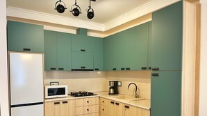 A kitchen with teal cabinets, a white refrigerator, a microwave, a stove, and a coffee maker. - City Heart Luxury Apartment  (Kutaisi)