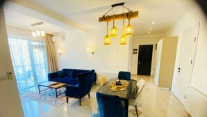 A modern living room with a blue sofa, a dining table with chairs, and a chandelier. - City Heart Luxury Apartment  (Kutaisi)