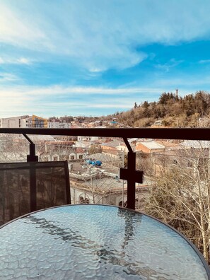 A balcony with a glass table and a view of a town with buildings and trees.