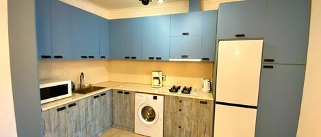 Una cocina compacta con armarios azules, lavadora, microondas, cafetera y refrigerador.