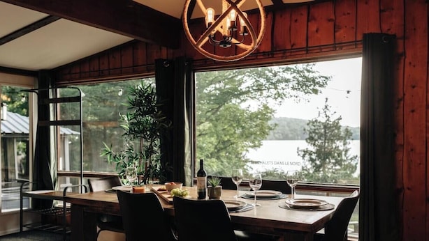 Un comedor con una mesa dispuesta para cuatro, una botella de vino y vistas a un lago.