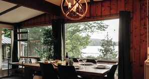A dining area with a table set for four, a bottle of wine, and a view of a lake. - Chalet à louer dans les Laurentides : spa privé + bord du lac à Sainte-Lucie-des-Laurentides (Sainte-Lucie des Laurentides)