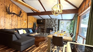 Acogedor interior de cabaña con sofá, mesa de comedor, chimenea y pared de piedra.