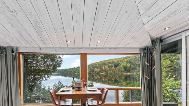 A dining area with a table set for two, a view of a lake, and a wooden ceiling.