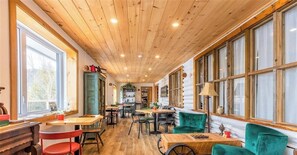 Un intérieur chaleureux avec des plafonds en bois, de grandes fenêtres et des fauteuils recouverts d’un tissu vert.