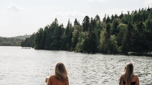 Two people facing a body of water with a forested shoreline.