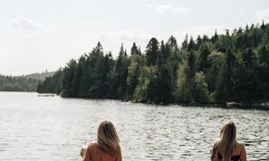 Deux personnes se tiennent face à une étendue d’eau, avec une rive bordée d’une forêt.