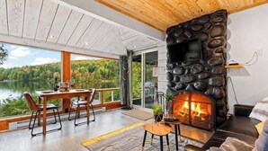 A modern interior with a stone fireplace, a dining area, and a view of a lake.