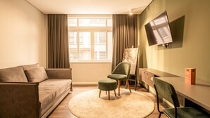 Un salon moderne comprenant un canapé, deux fauteuils, une petite table, un téléviseur fixé au mur et une fenêtre avec des rideaux.