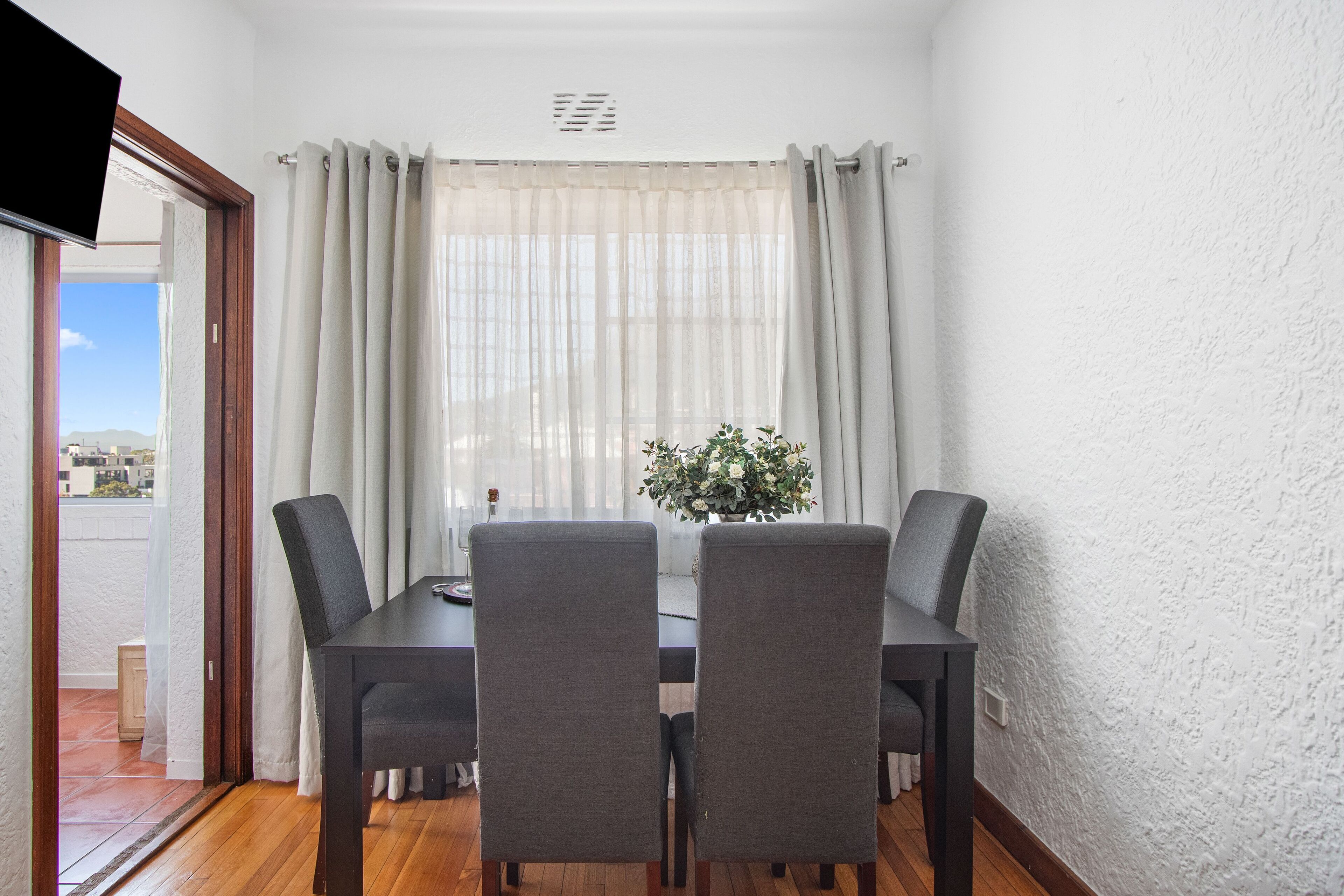 Un coin repas avec une table et des chaises, une fenêtre avec des rideaux et une vue sur l’extérieur.
