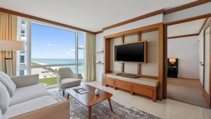 Een hotelkamer met een groot raam, een flatscreen televisie, een bank, een bijzettafeltje en een klein kastje.