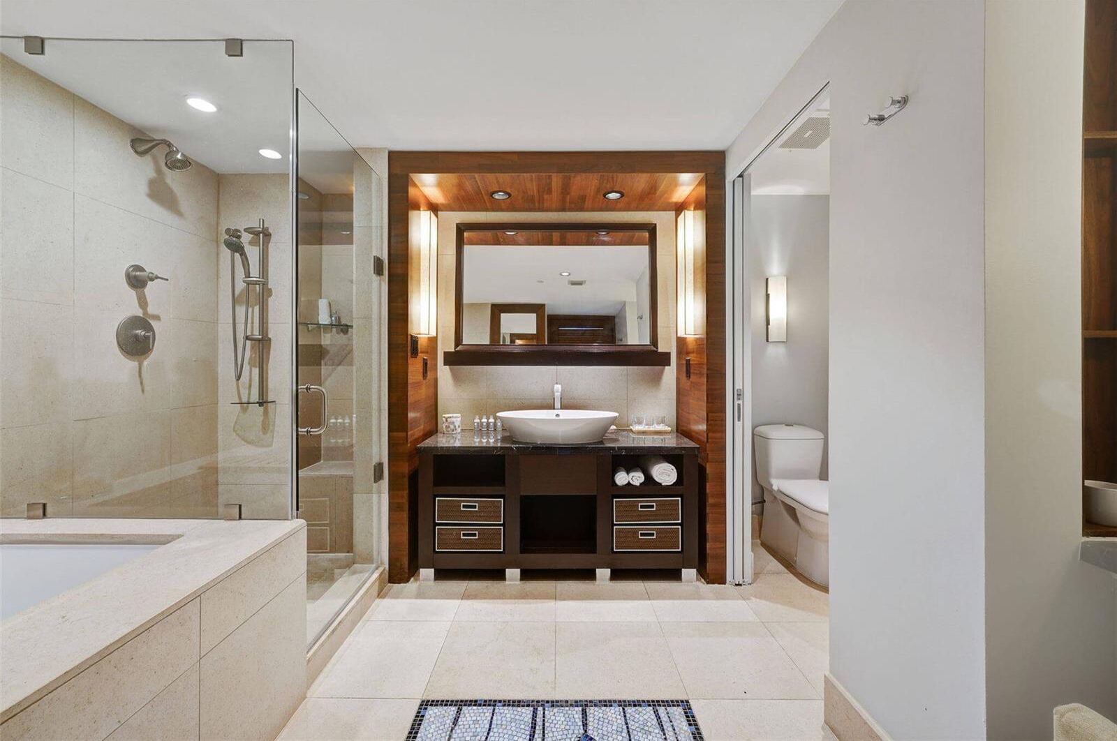 Un baño moderno con ducha envuelta en vidrio, un lavamanos grande y un mueble de tocador de madera.
