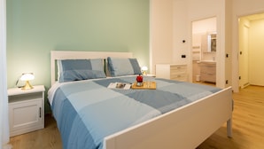 A neatly made bed with a blue and white bedspread, a bedside table with a lamp, and a tray with a red cup and glasses. - Italianflat - Vittoria Suite (Milan)