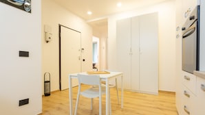 A modern kitchen with white cabinets, a wooden floor, and a dining area with a white table and chairs. - Italianflat - Vittoria Suite (Milan)