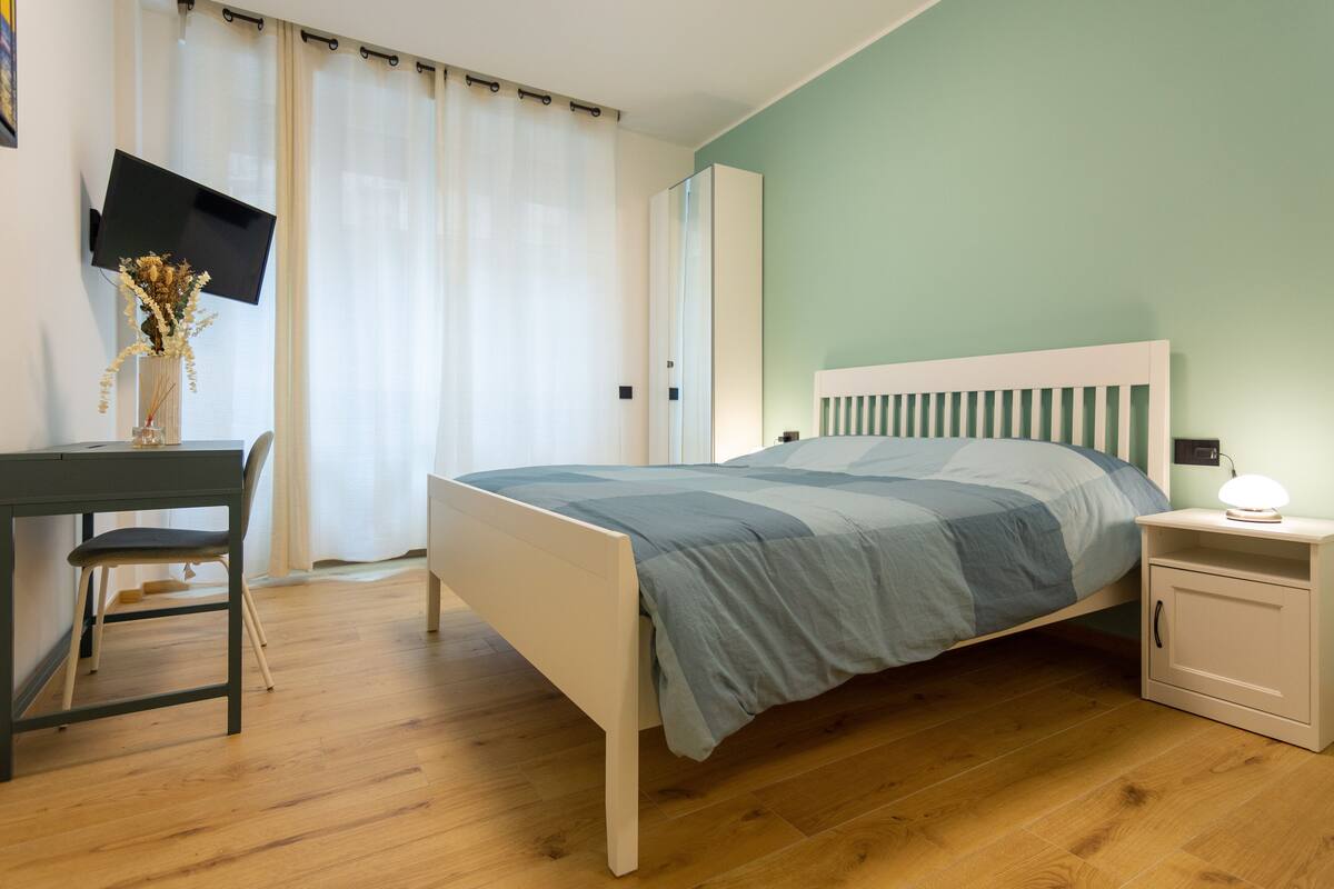 A bedroom with a bed, bedside table, and a desk with a chair.