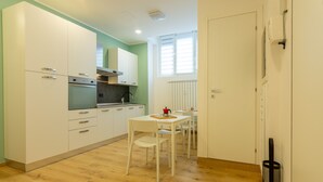 A compact kitchen with white cabinets, a built-in oven, and a dining area with a table and chairs. - Italianflat - Vittoria Suite (Milan)