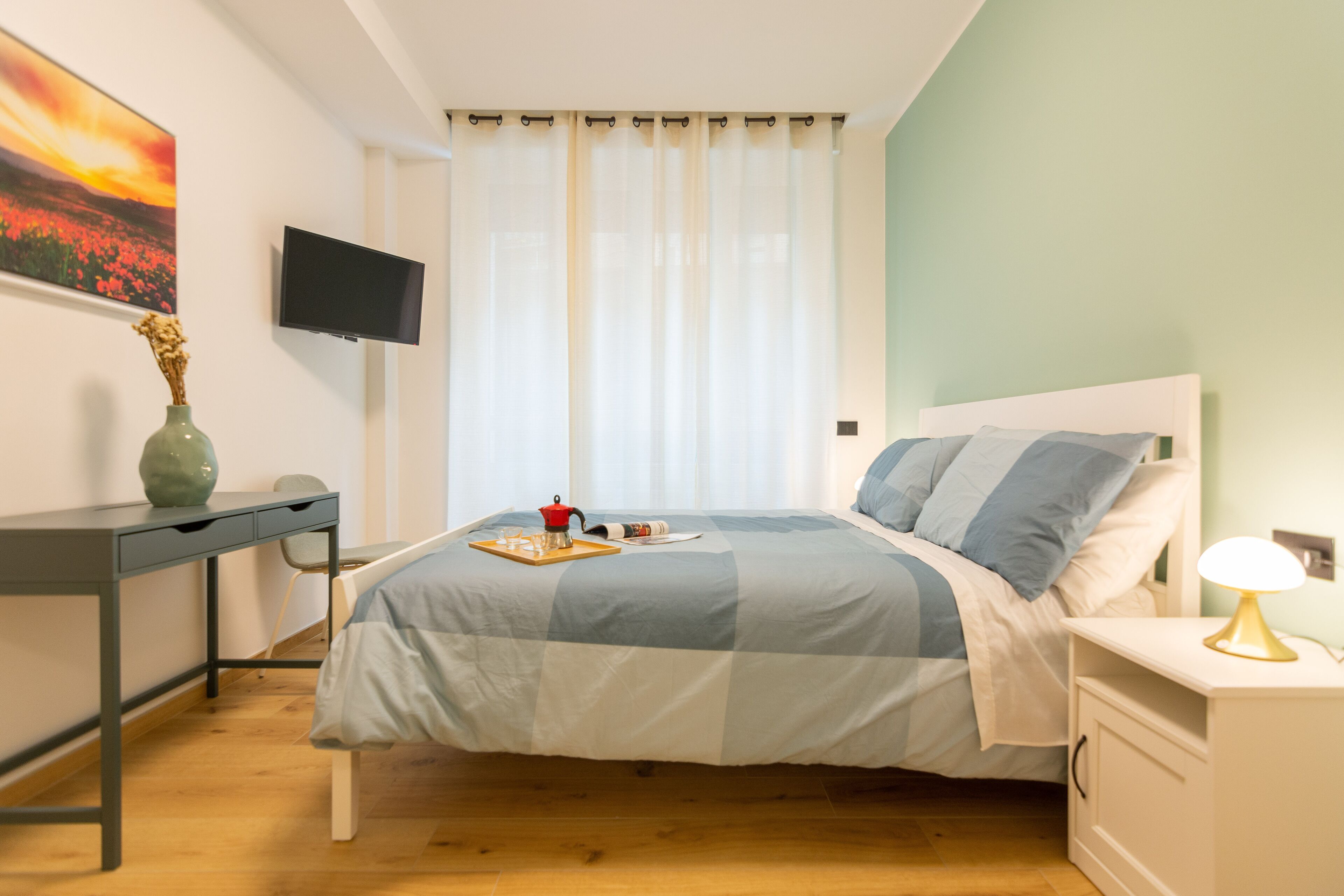 Een slaapkamer met een bed, een bureau, een televisie en een nachtkastje.