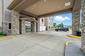 Entrada de hotel com pilares de pedra, galeria coberta e área de estacionamento.