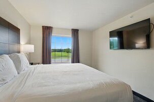 A hotel room with a large bed, a flat-screen TV mounted on the wall, and a window with curtains.