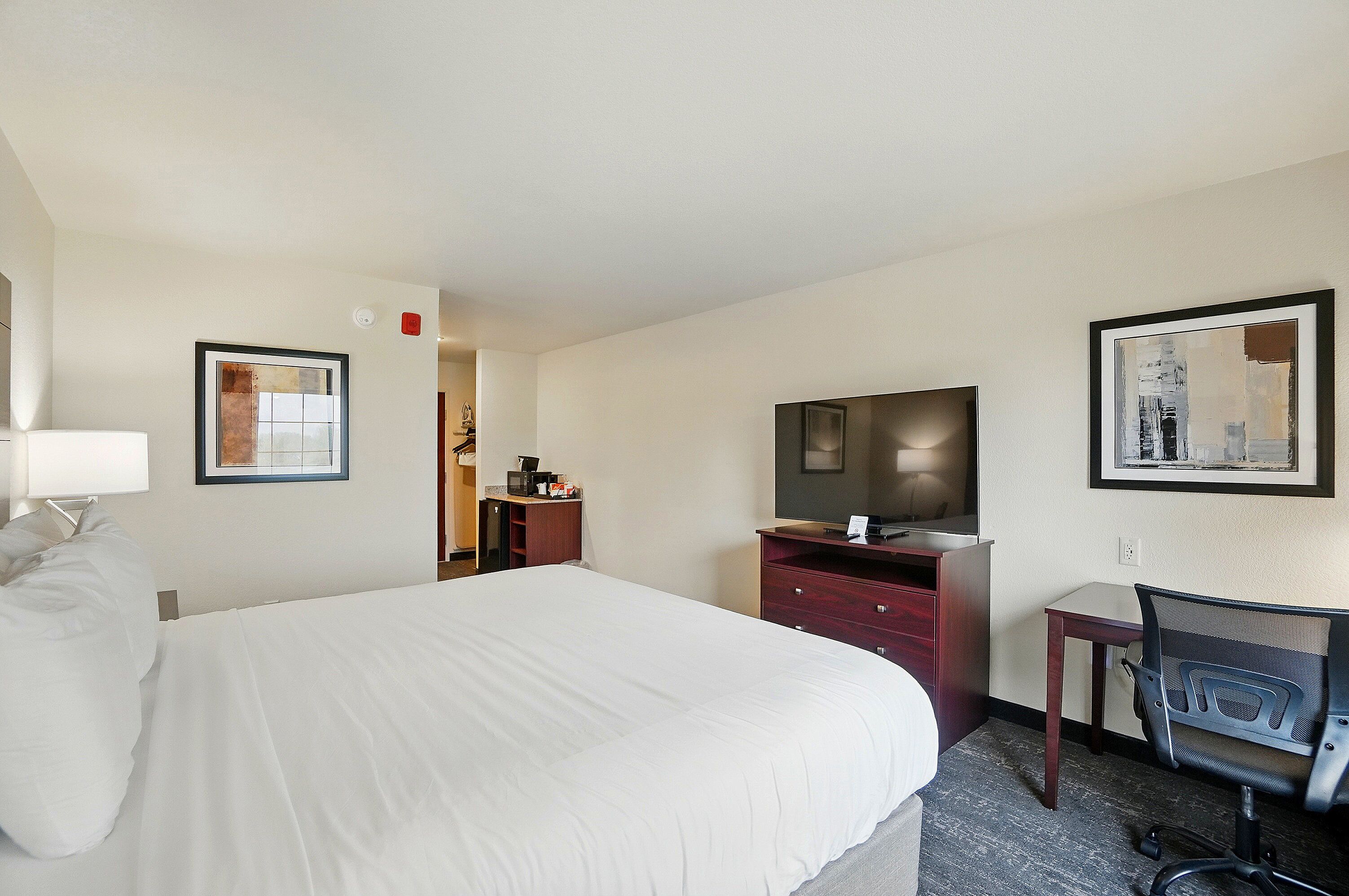 Habitación de hotel con una cama grande, un escritorio con silla, televisión y obras de arte en las paredes.