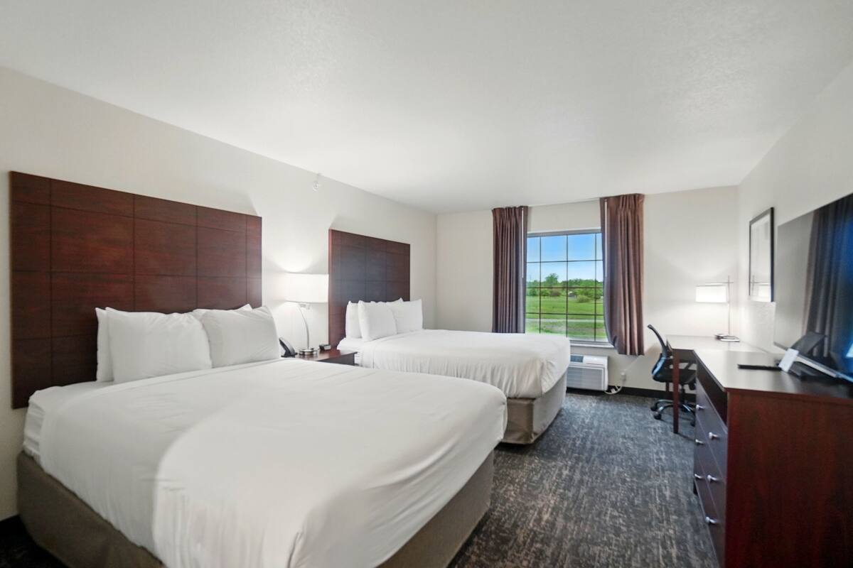 A hotel room with two beds, a desk, a chair, a TV, and a window with curtains.