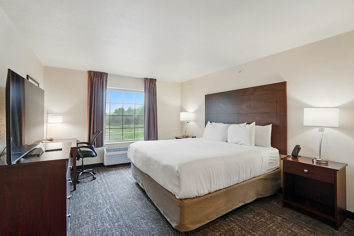 A hotel room with a large bed, a desk with a chair, a TV, and a window with curtains.
