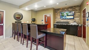 A modern kitchen with a bar area, a television, and a stone accent wall. - Cobblestone Hotel & Suites-RussellsPoint (Russells Point)