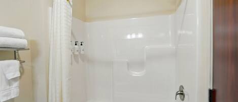 A shower area with a glass door, a towel rack with towels, and a showerhead.