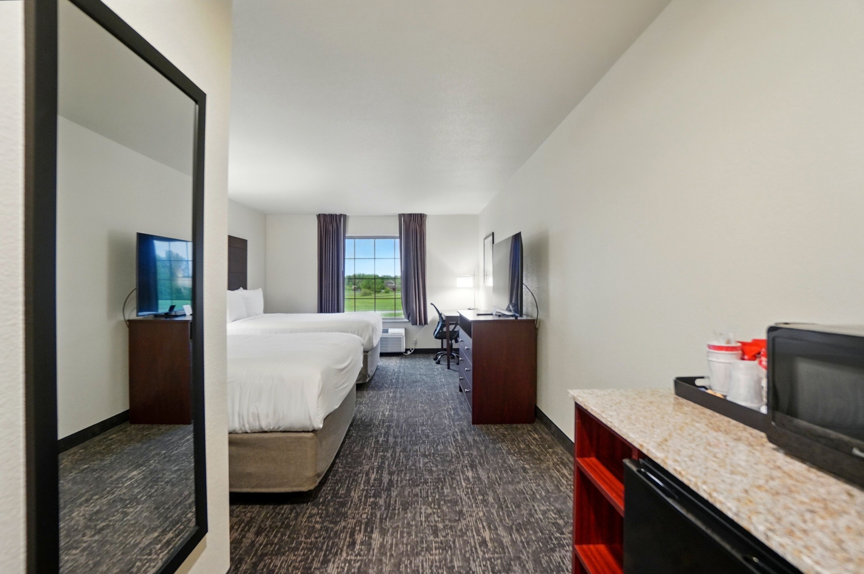 Een hotelkamer met twee bedden, een bureau, een televisie en uitzicht op de omgeving.