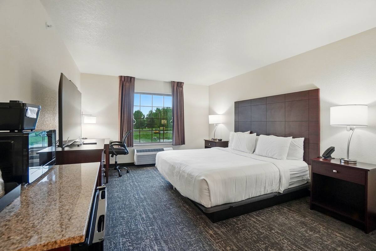 A hotel room with a bed, desk, chair, and a large window with curtains.