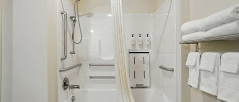 Un baño moderno con bañera, ducha y barras de apoyo. Hay toallas en un perchero y dispensadores de jabón en la pared.