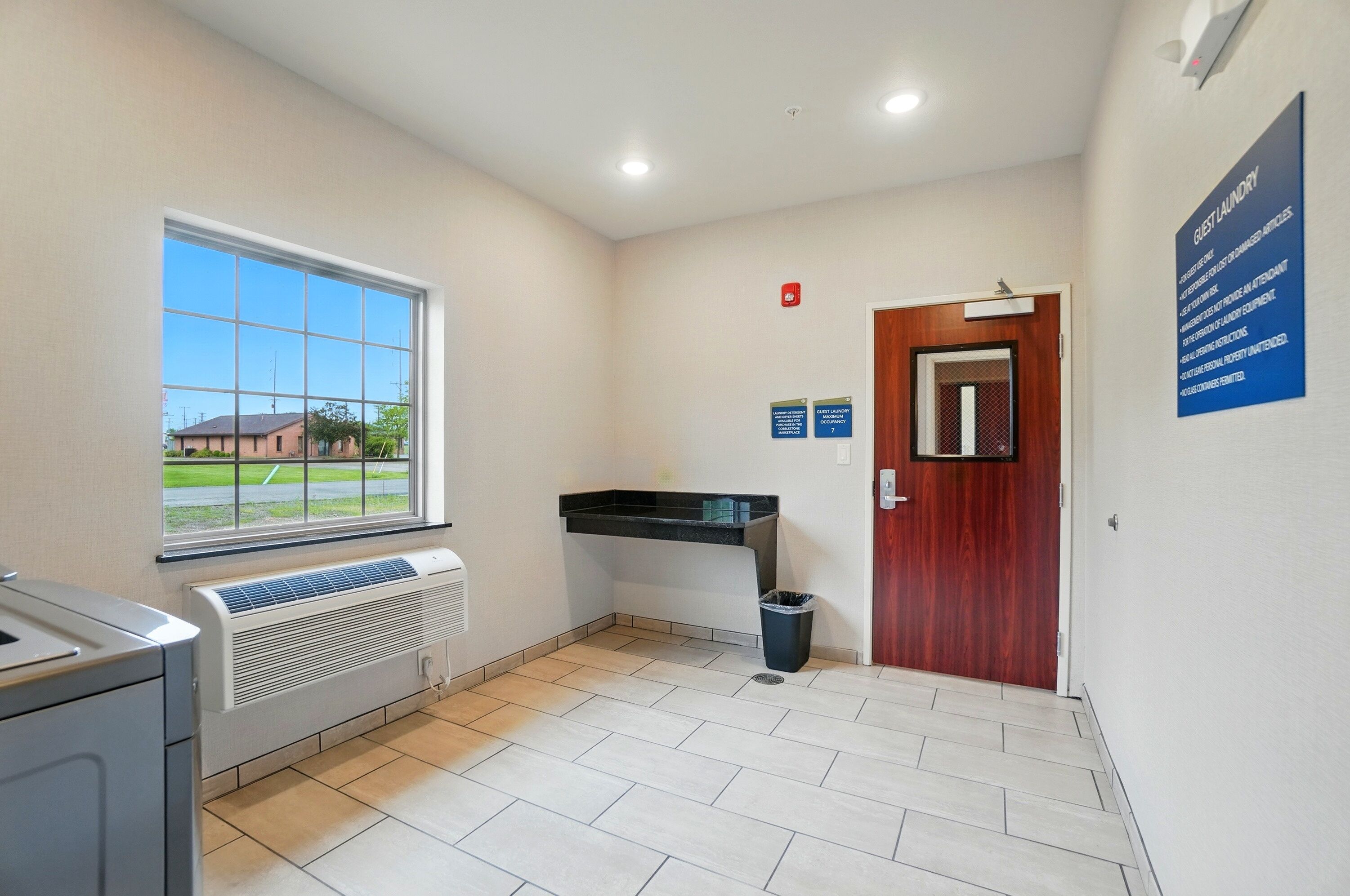 A laundry room with a large window, a sink, a heater, and a door.