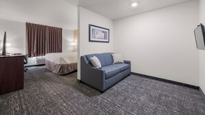 A hotel room with a bed, a desk, a blue sofa, and a framed picture on the wall. - Cobblestone Hotel & Suites-RussellsPoint (Russells Point)