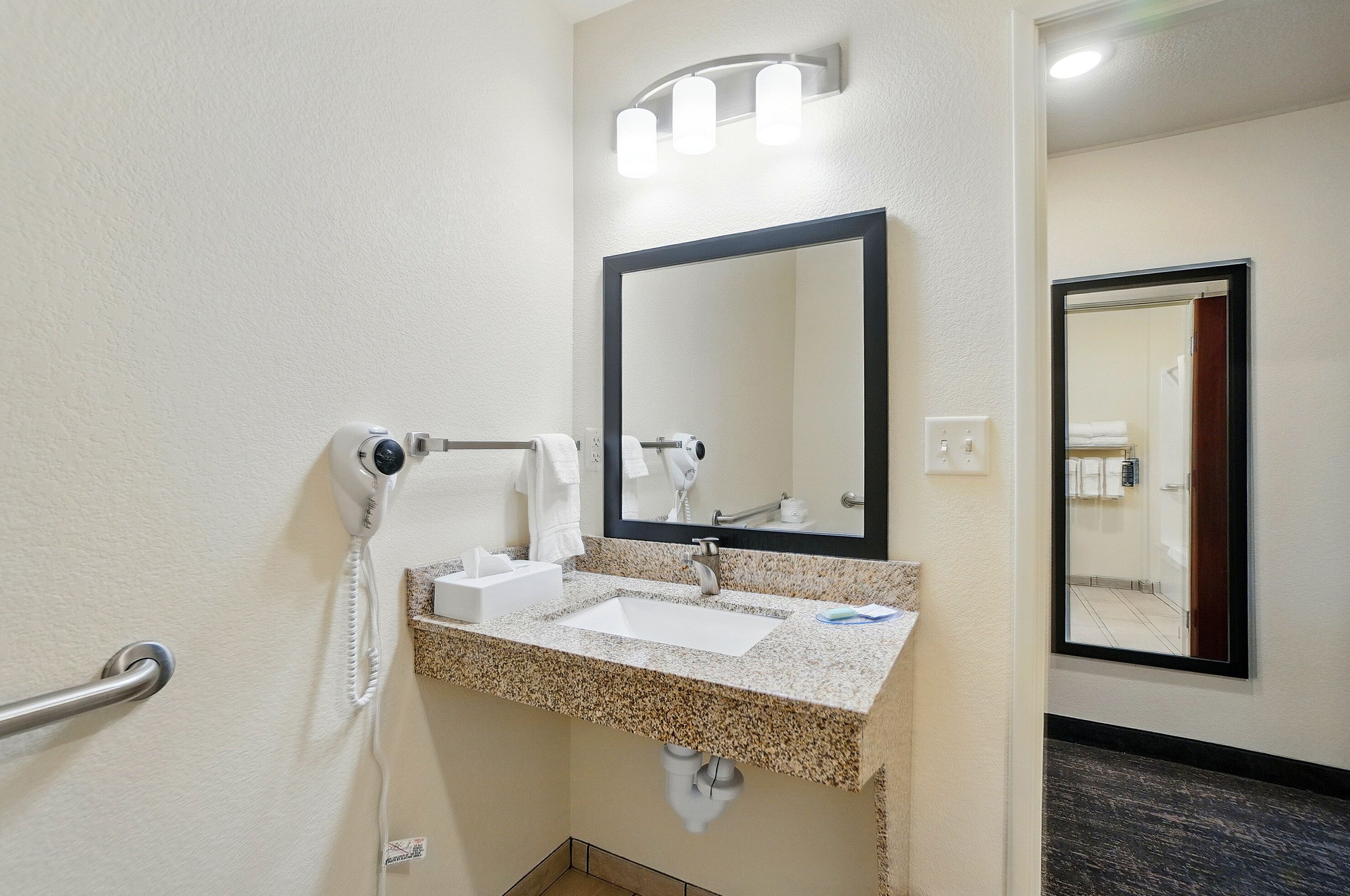 Un baño de hotel con lavamanos, espejo y dispensador de toallas.