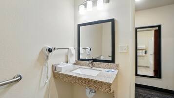Un baño de hotel con lavamanos, espejo y dispensador de toallas.