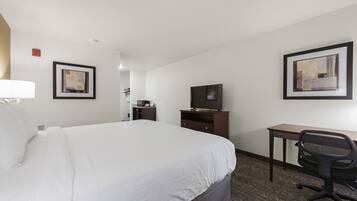 Habitación de hotel con una cama grande, un escritorio con silla, un televisor y obras de arte en las paredes.